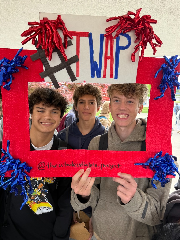 Three male student-athletes posing with a TWAP photo frame sign