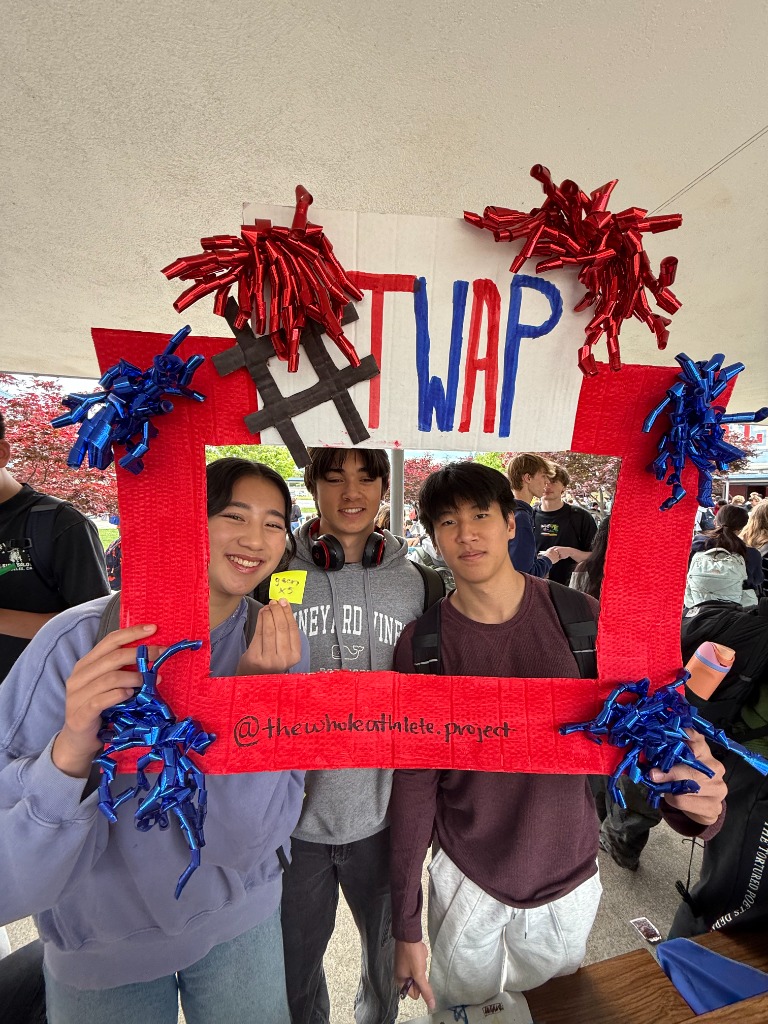 Three male students posing with a TWAP photo frame sign at a campus event